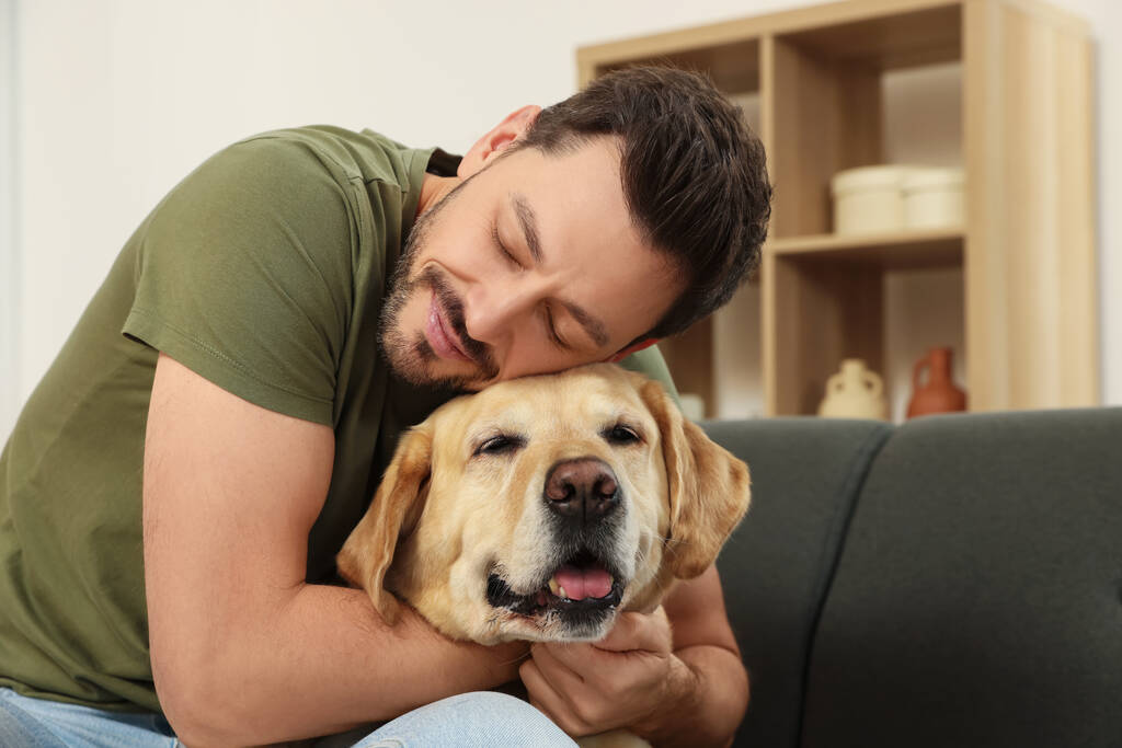 Mann umarmt seinen niedlichen Labrador Retriever zu Hause auf dem Sofa. Raum für Text - Foto, Bild