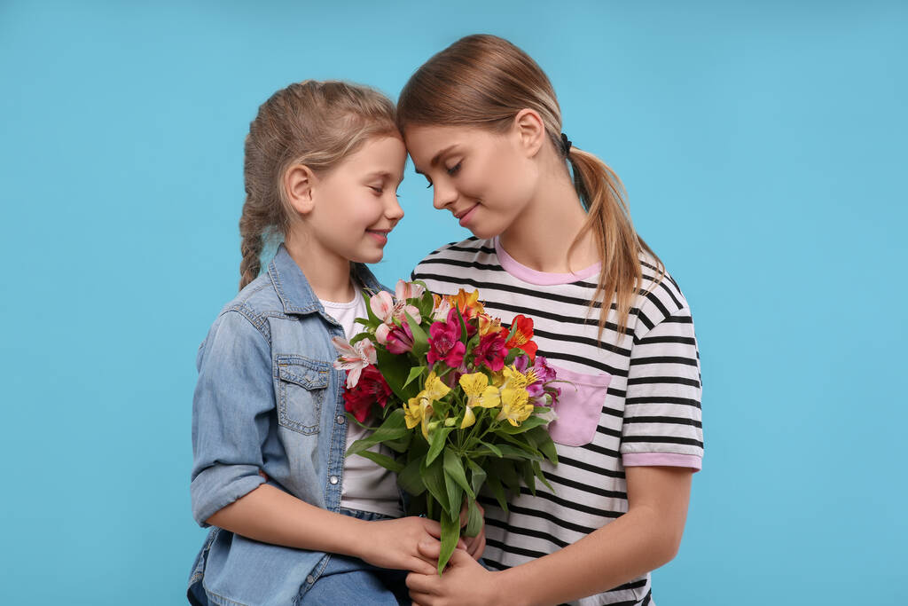 Kleine dochter feliciteert haar moeder met bloemen op lichtblauwe achtergrond. Gelukkige Moederdag - Foto, afbeelding
