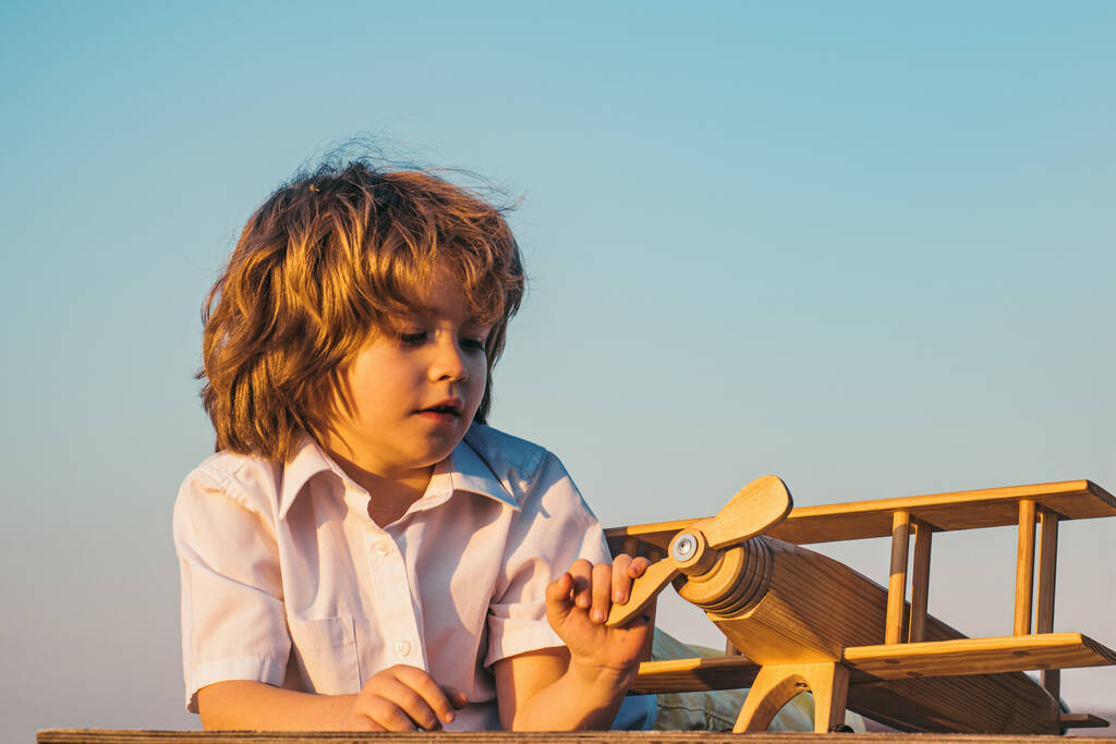 Дитячий хлопчик грає з дерев'яним іграшковим літаком, мріє стати пілотом. Дитячі сни. Дитячий льотчик-авіатор з дерев'яною площиною
 - Фото, зображення