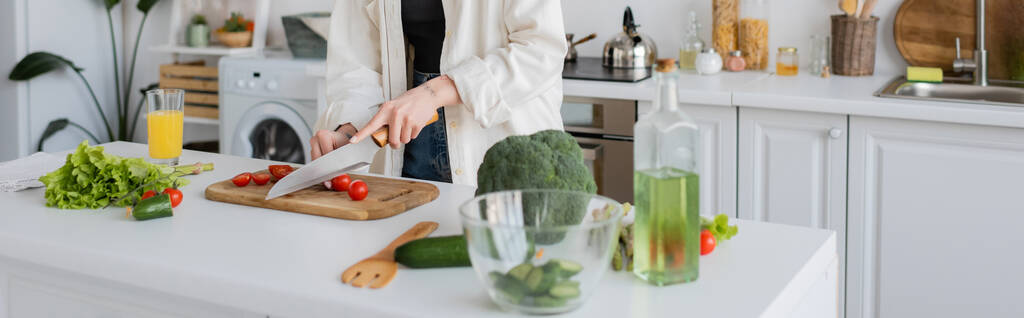 Vista recortada de la joven mujer cortando tomates cherry cerca de verduras y jugo de naranja en la cocina, pancarta  - Foto, imagen
