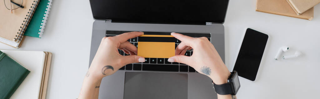 Visão superior da mulher tatuada segurando cartão de crédito perto de gadgets e notebooks na mesa, banner  - Foto, Imagem