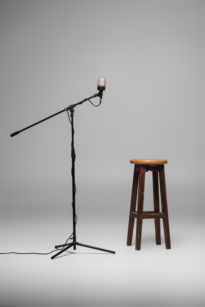 Hnědá dřevěná židle stojící poblíž černého mikrofonu na kovovém stojanu na šedém pozadí s kopírovacím prostorem, vysoká stolička ve studiu  - Fotografie, Obrázek