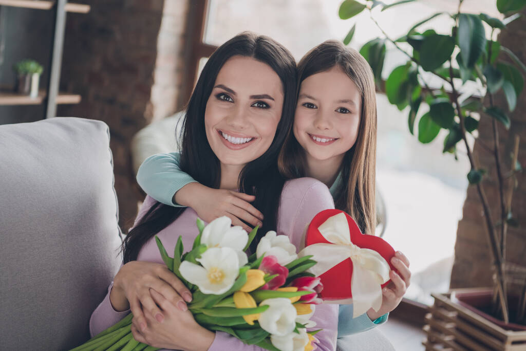 Portret kochającej rodziny dziecko dziewczyna świętować dzień matki uścisk objąć mamusia dać kwiat bukiet prezent pudełko w mieszkaniu. - Zdjęcie, obraz
