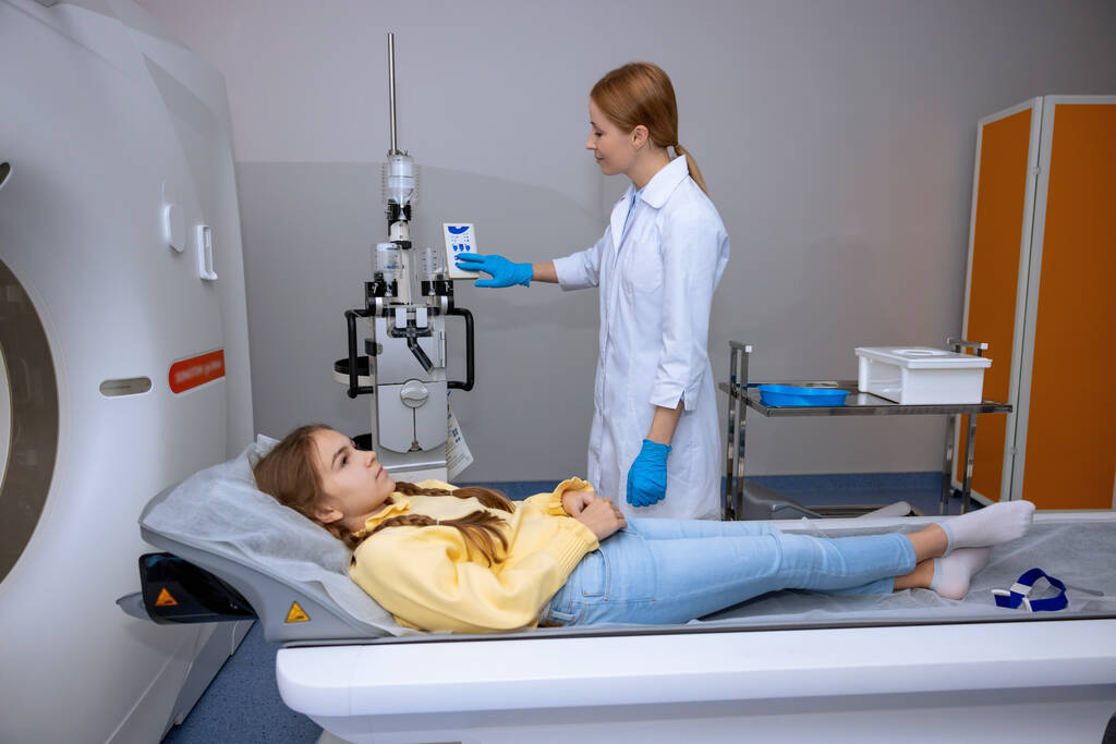 Kislány beteg fekszik a hosszú orvosi asztalon az MRI vizsgálat során a kórházban, orvos csinál tomográfia gyermek egy klinikán. - Fotó, kép