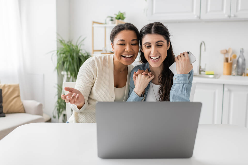 happy interracial lgbt couple holding hands and smiling during video call  - Photo, Image