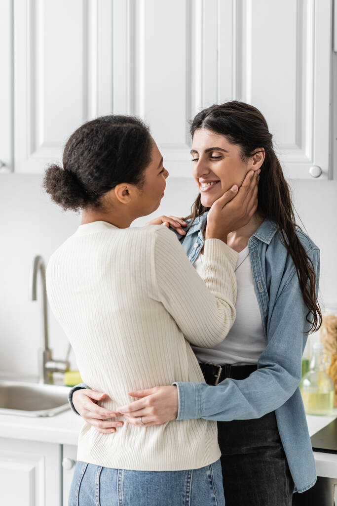 mulher lésbica satisfeito abraço com namorada multirracial na cozinha moderna  - Foto, Imagem