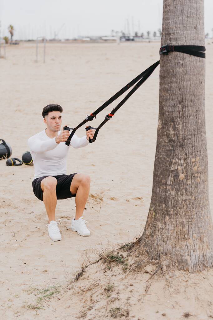Спортивний молодий іспанський самець робить вправи на плечах з мотузкою на пляжі. - Фото, зображення