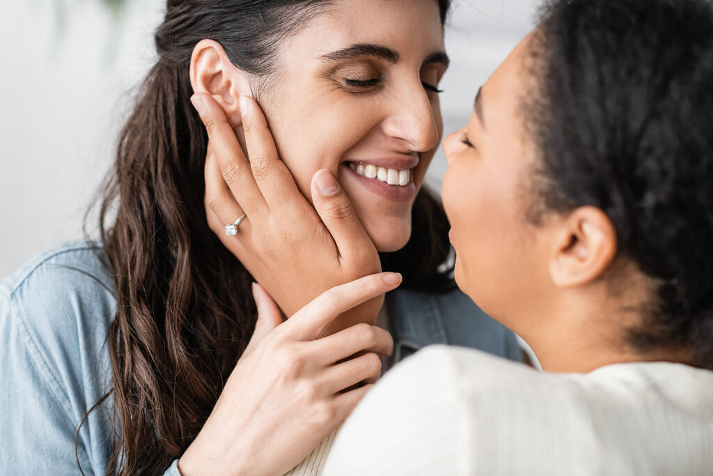femme multiraciale ravie avec bague de fiançailles sur doigt étreignant petite amie souriante  - Photo, image