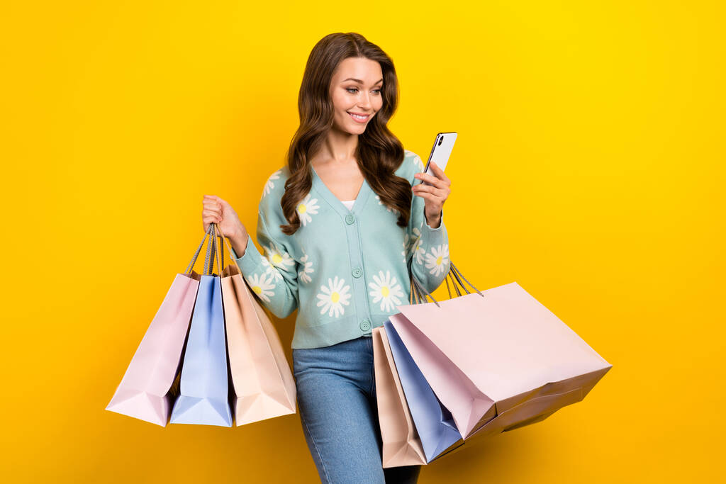 Πορτρέτο του χαρούμενα πανέμορφο κορίτσι κρατήσει τσάντες εμπορικό κέντρο χρησιμοποιούν τηλέφωνο απομονωμένο σε κίτρινο χρώμα φόντο. - Φωτογραφία, εικόνα