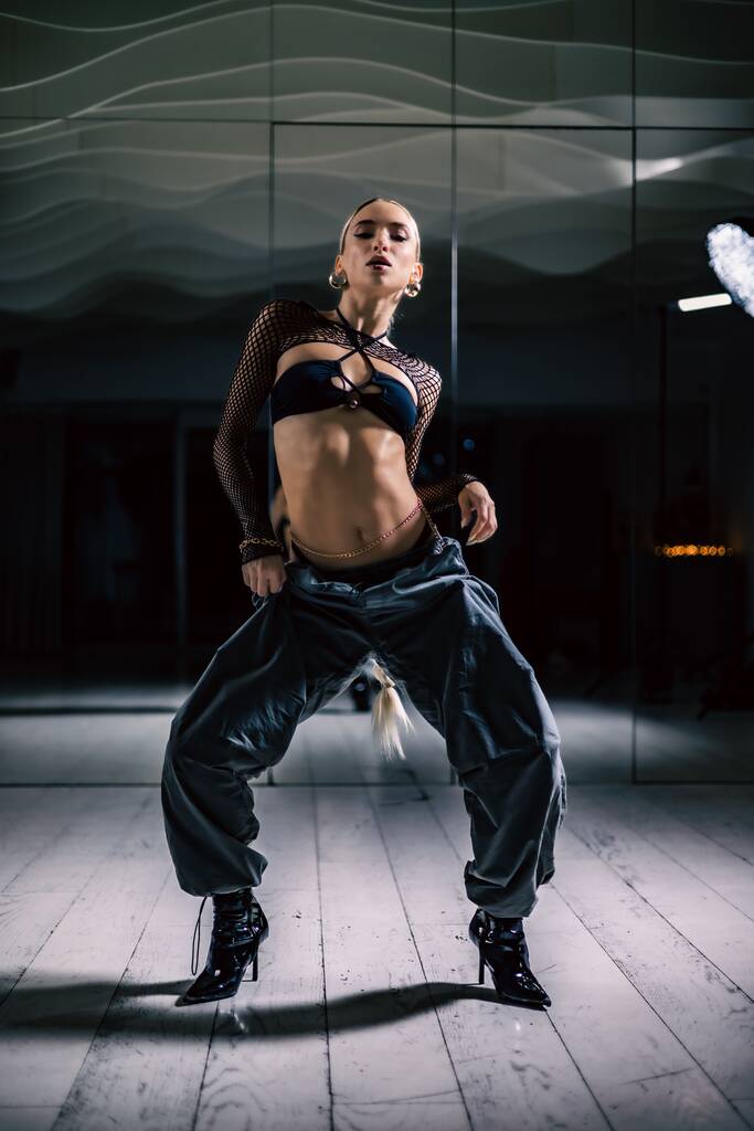 Eine vertikale Aufnahme einer schönen Tänzerin posiert in Mesh-Overlay Crop Top in schwarzen und sackartigen Hosen - Foto, Bild