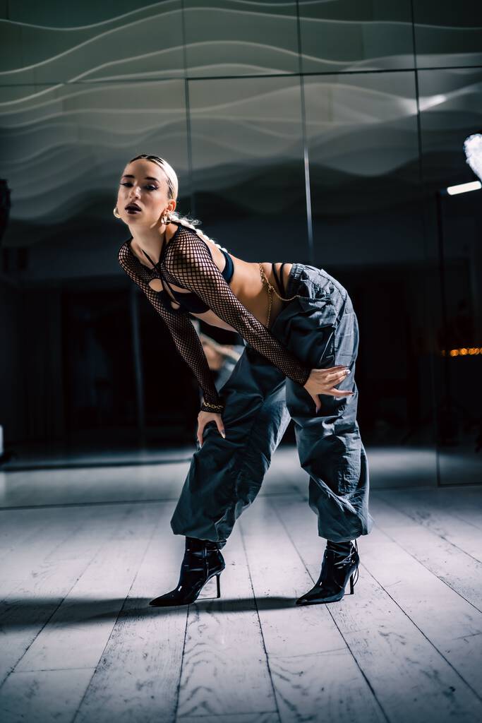 Een verticaal schot van een mooie vrouwelijke danser poseren in mesh overlay gewas top in zwart en baggy broek - Foto, afbeelding