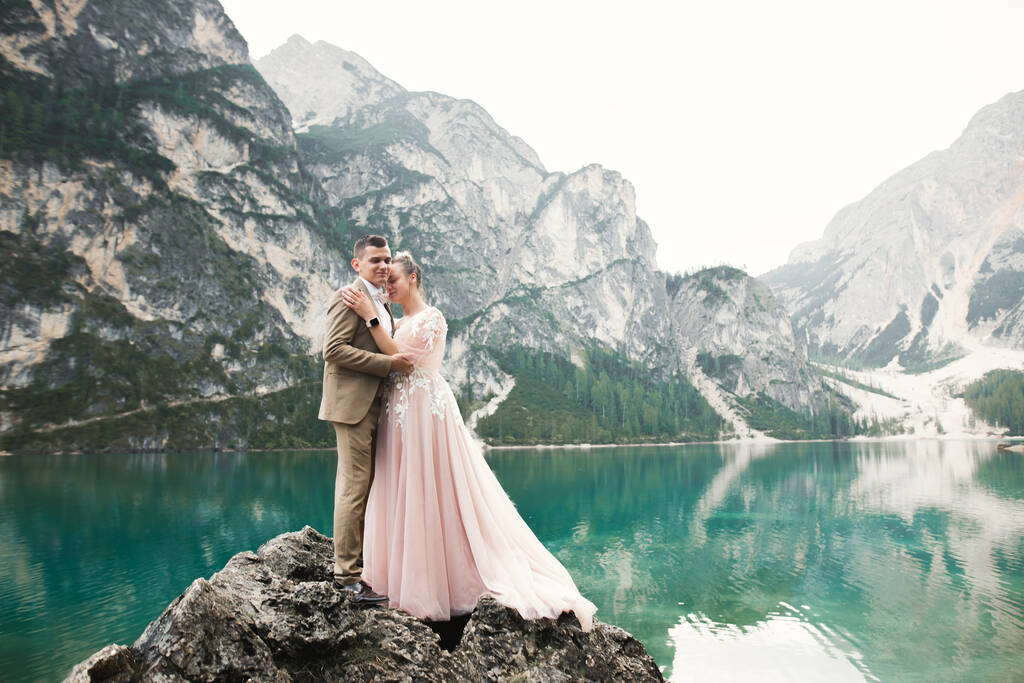 Bruidspaar op de natuur knuffelt elkaar in de buurt van een prachtig meer in de bergen.. Mooi model meisje in witte jurk. Man in pak. - Foto, afbeelding