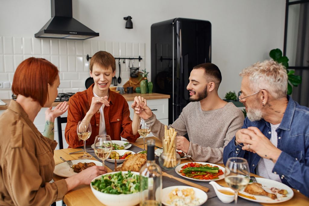 bärtiger schwuler Mann hält Hand eines rothaarigen Freundes und zeigt Eltern Ehering während des Abendessens in der Küche - Foto, Bild