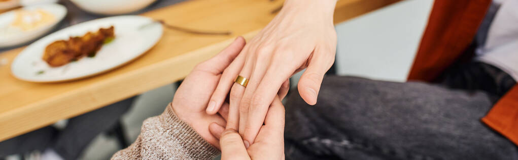 ostříhaný pohled na gaye držícího se za ruku přítele se snubním prstenem při podání nabídky k sňatku v kuchyni, banner - Fotografie, Obrázek