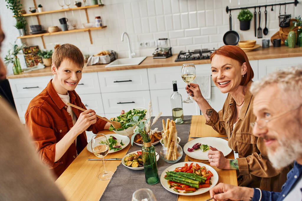 szczęśliwy gej człowiek z rodzice patrząc na zamazany chłopak mając pyszne kolacja w kuchnia - Zdjęcie, obraz