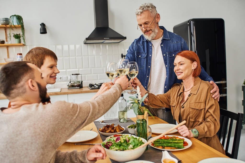 junges schwules Paar klappert Weingläser mit Eltern beim Abendessen in der modernen Küche - Foto, Bild