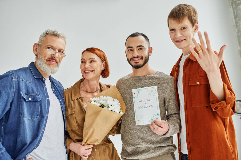 happy gay man showing wedding ring near parents with flowers and boyfriend with wedding invitation - Photo, Image