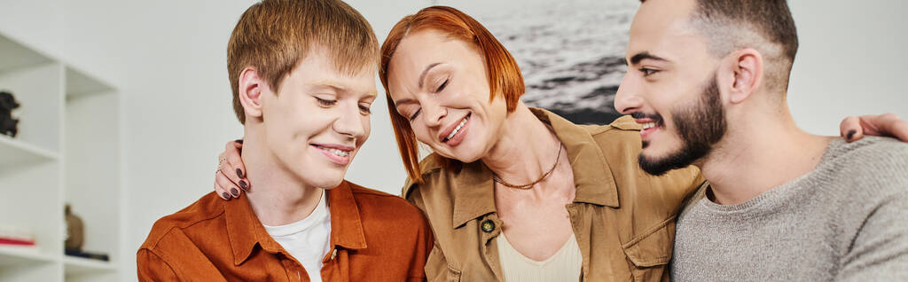 radosna kobieta z zamkniętymi oczami obejmująca uśmiechniętego geja i syna w domu, sztandar - Zdjęcie, obraz