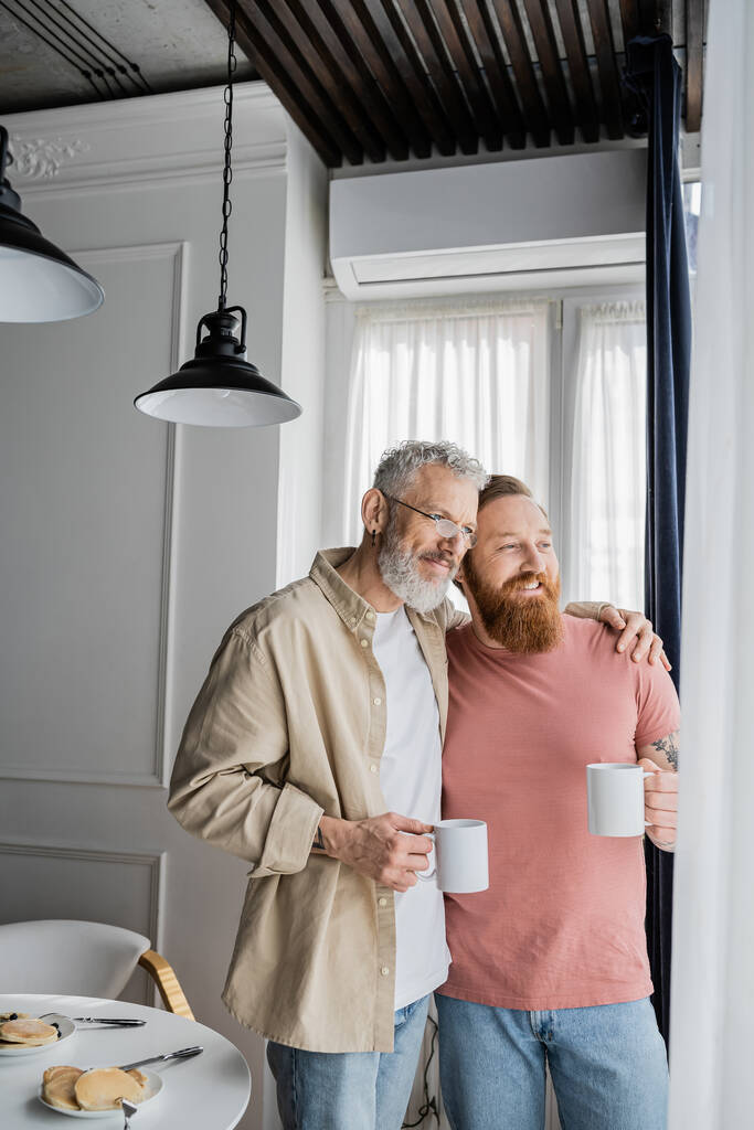 Mature gay homme câlin gai partenaire avec café près du petit déjeuner à la maison  - Photo, image