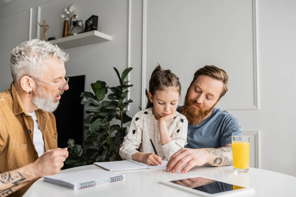 Γονείς του ίδιου φύλου κάνουν την εργασία με την κόρη γράφοντας στο σημειωματάριο στο σπίτι  - Φωτογραφία, εικόνα
