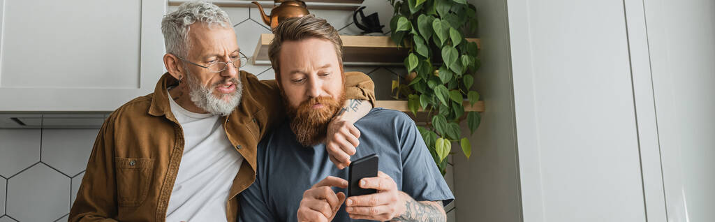 Homoseksuaali mies halaus kumppani käyttäen matkapuhelin keittiössä, banneri  - Valokuva, kuva
