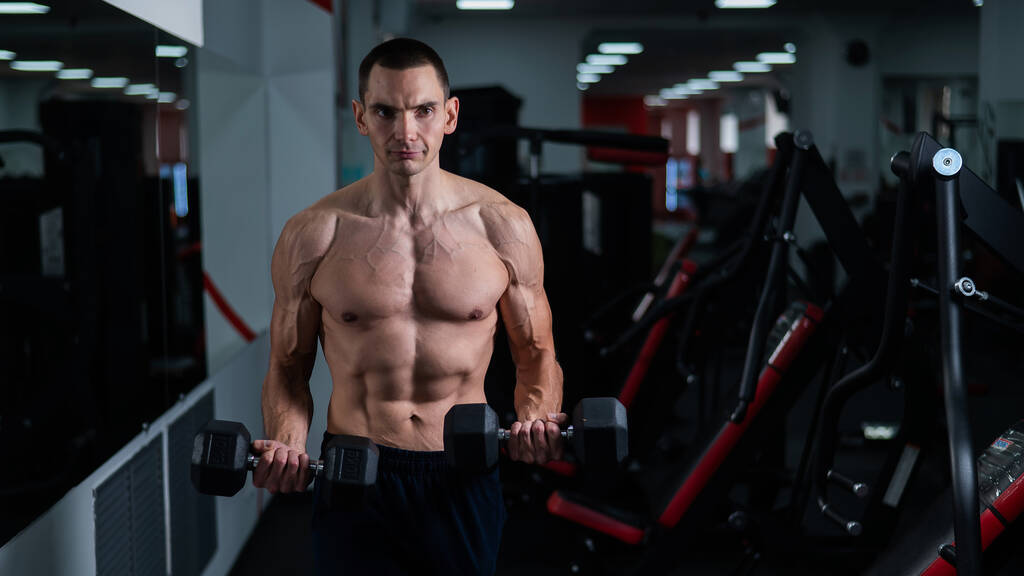 Shirtless man doing bicep exercises with dumbbells in the gym - Photo, image