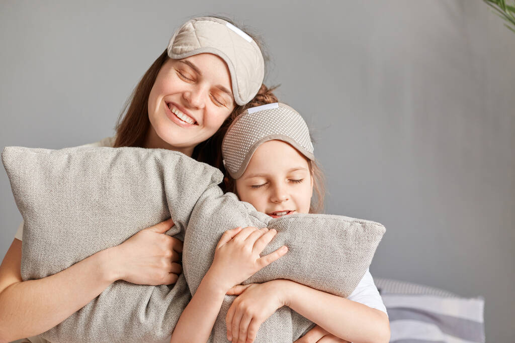 Portrait de mère avec sa jolie petite fille assise sur le lit les yeux fermés faisant la sieste en profitant du week-end somnolence souriant avec des visages heureux. - Photo, image