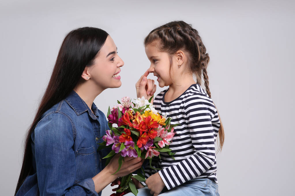 Mujer feliz con su linda hija y ramo de hermosas flores sobre fondo gris claro. Celebración del día de la madre - Foto, Imagen