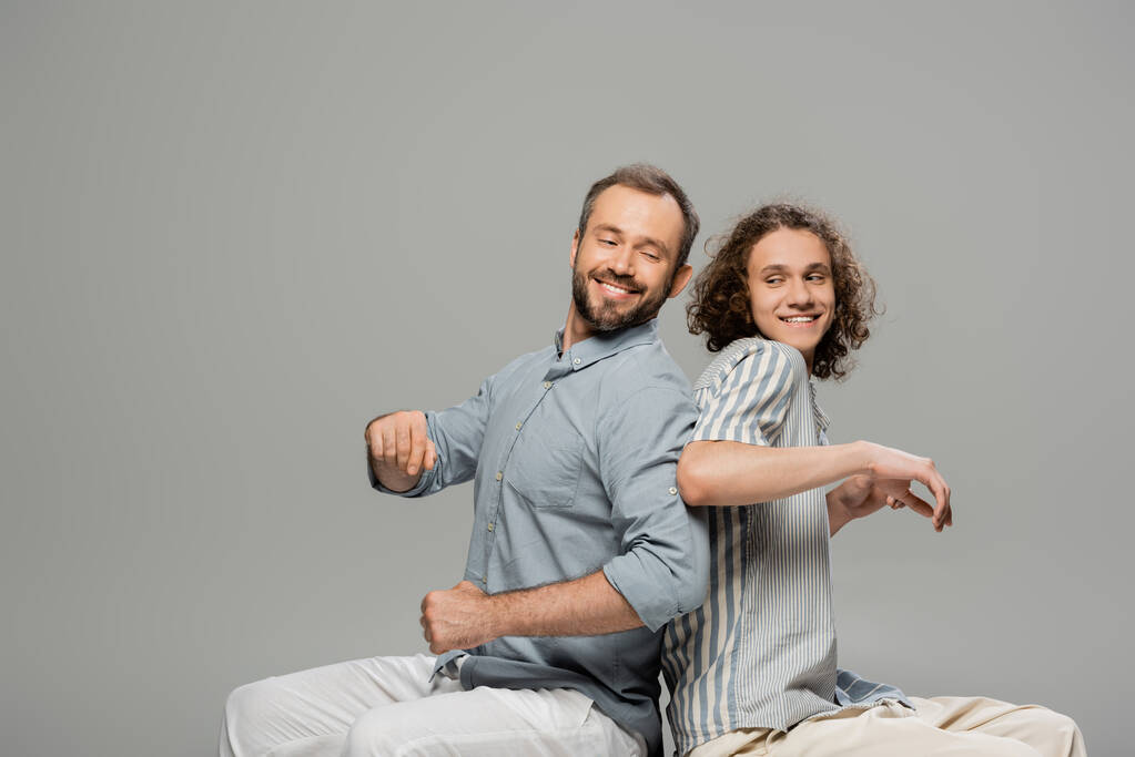 happy father and son having fun and pushing each other while sitting isolated on grey  - Photo, Image