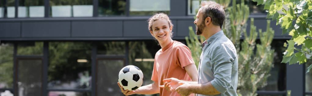 Mutlu genç çocuk futbol topunu tutuyor ve dışarıda yürürken babasına bakıyor.  - Fotoğraf, Görsel