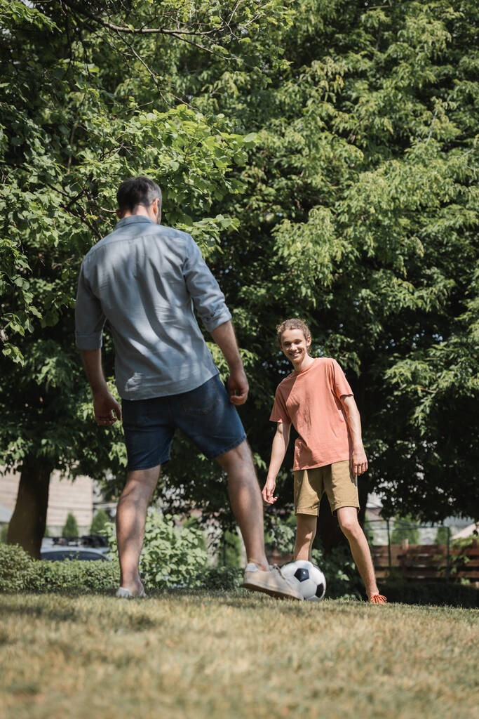 onnellinen teini-ikäinen poika pelaa jalkapalloa isänsä kanssa vihreässä kesäpuistossa  - Valokuva, kuva