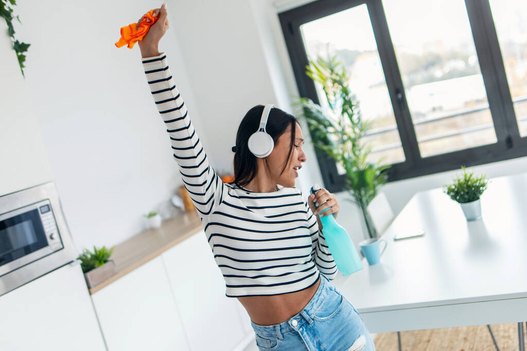 Foto de hermosa mujer feliz cantando y bailando mientras se limpia la cocina en casa - Foto, imagen