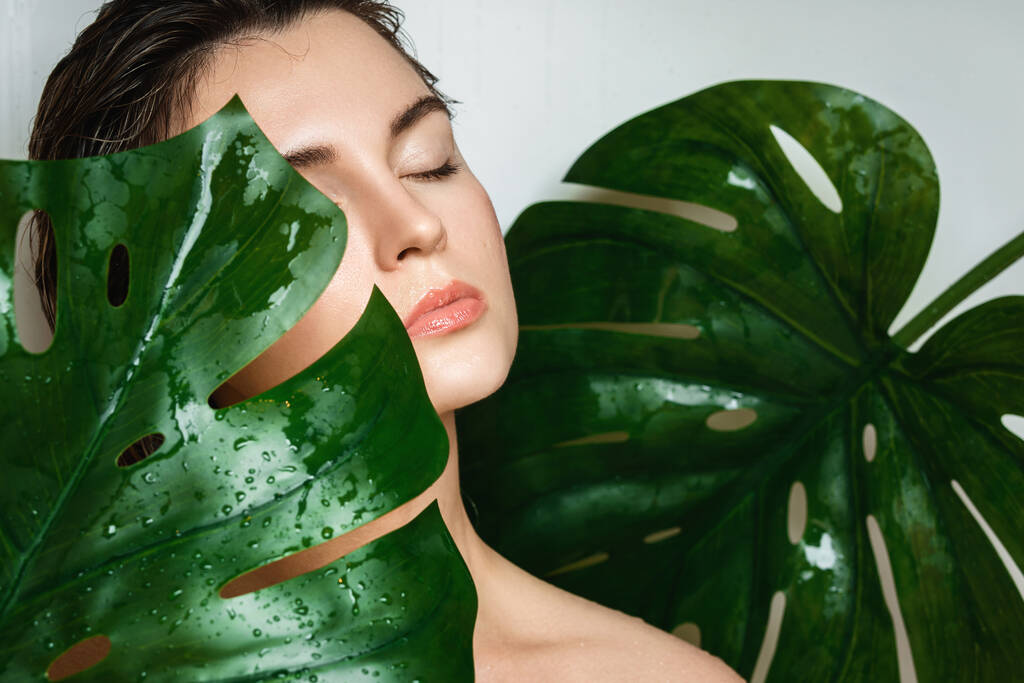 Portret van een mooie jonge vrouw met een gladde huid met Monstera deliciosa plantenblad - Foto, afbeelding