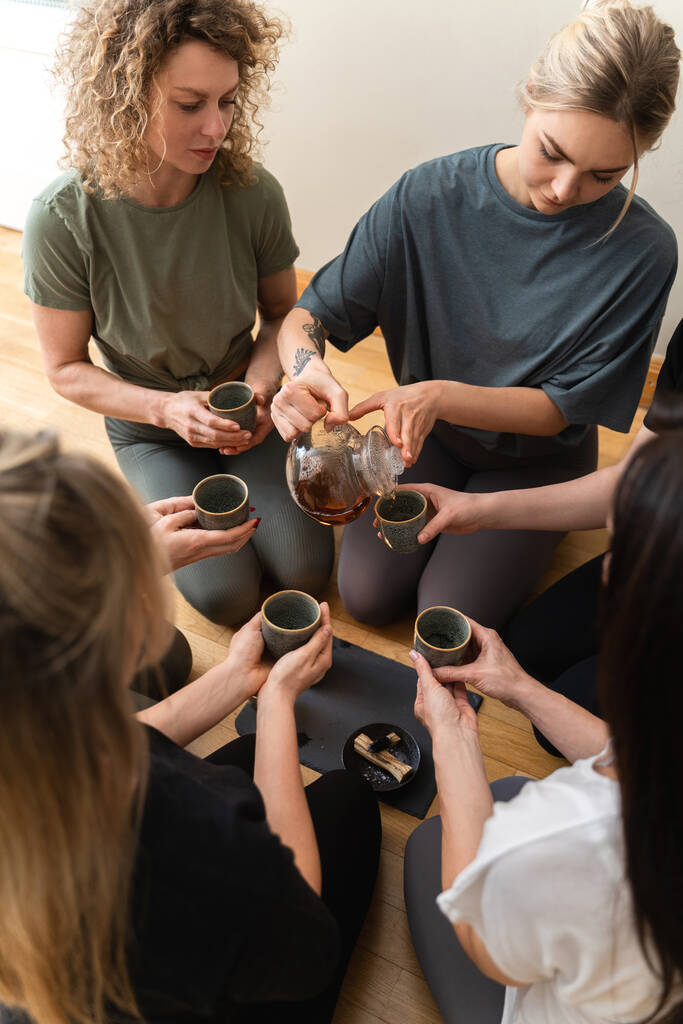 Mujer joven está sirviendo té caliente a sus amigos sentados alrededor de una bandeja durante una ceremonia de té. - Foto, Imagen
