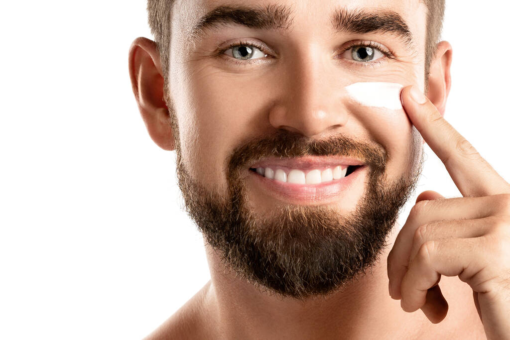Pánské krásy - Mladý muž je nanášení hydratační a proti stárnutí krém na tváři proti bílému pozadí - Fotografie, Obrázek