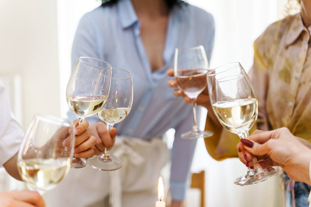 Beyaz şarapla dolu kadehleri tokuşturan genç kadınların yakın çekimi. - Fotoğraf, Görsel