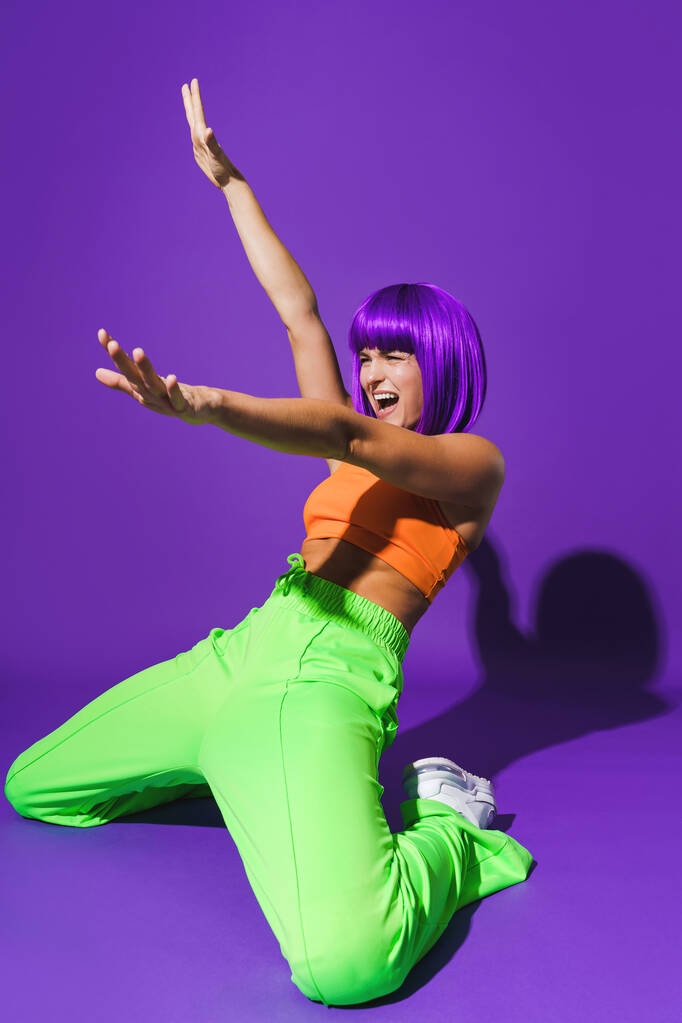 Carefree active woman dancer wearing colorful sportswear performing against purple background - Photo, Image