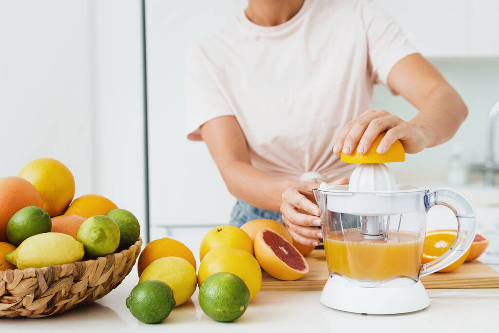 新鮮なオレンジジュースの準備中に女性の手と柑橘類のジューサーの閉鎖 - 写真・画像