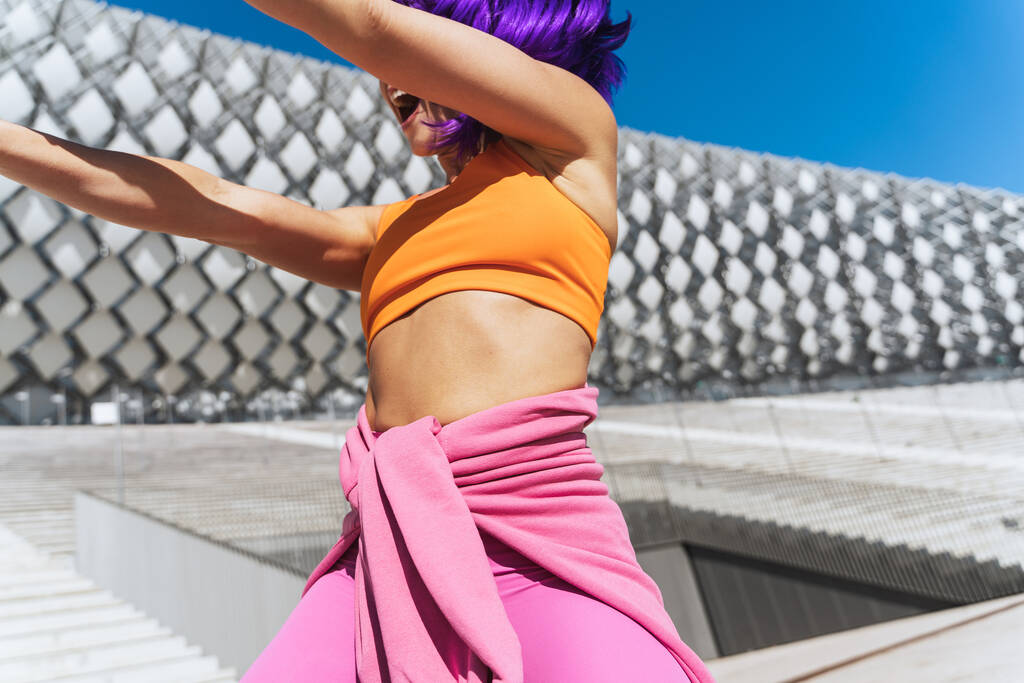 Femme active insouciante danseuse portant des vêtements de sport colorés s'amusant dans la rue pendant la journée ensoleillée - Photo, image