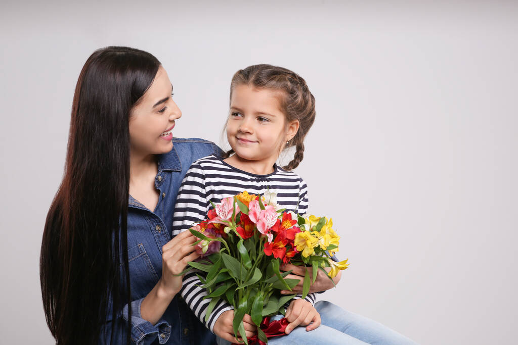 Femme heureuse avec sa fille mignonne et bouquet de belles fleurs sur fond gris clair, espace pour le texte. Fête des mères - Photo, image