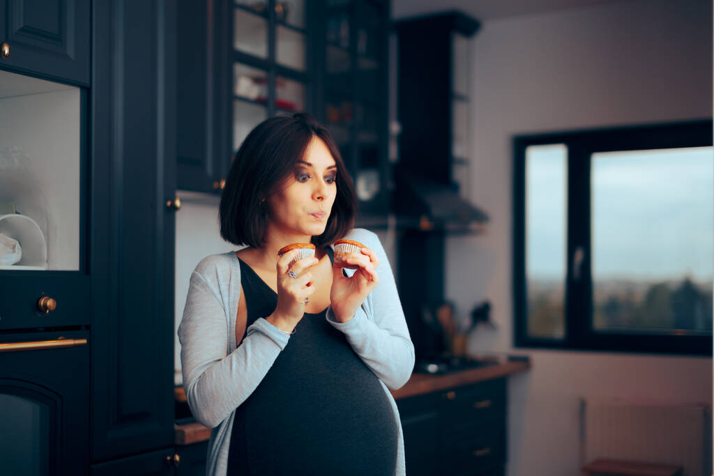 Grappige zwangere vrouw met muffins in de keuken  - Foto, afbeelding