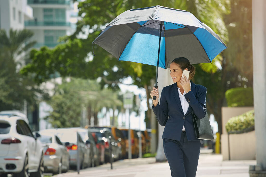 Chrání její obchodní zájmy. mladá podnikatelka, která mluví po telefonu a drží ve městě deštník - Fotografie, Obrázek
