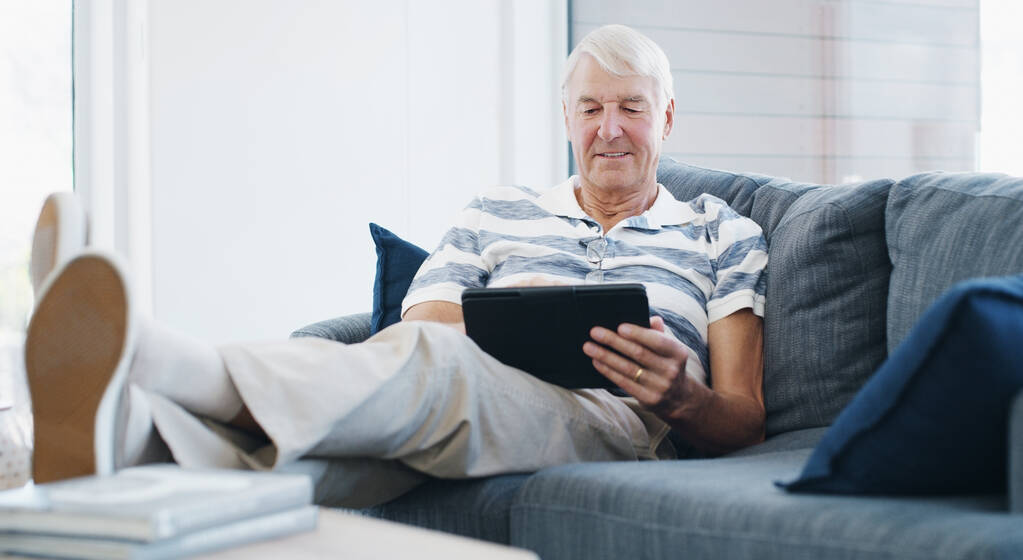 Het is een eenvoudiger wereld dankzij slimmere technologie. een oudere man die thuis een digitale tablet op de bank gebruikt - Foto, afbeelding