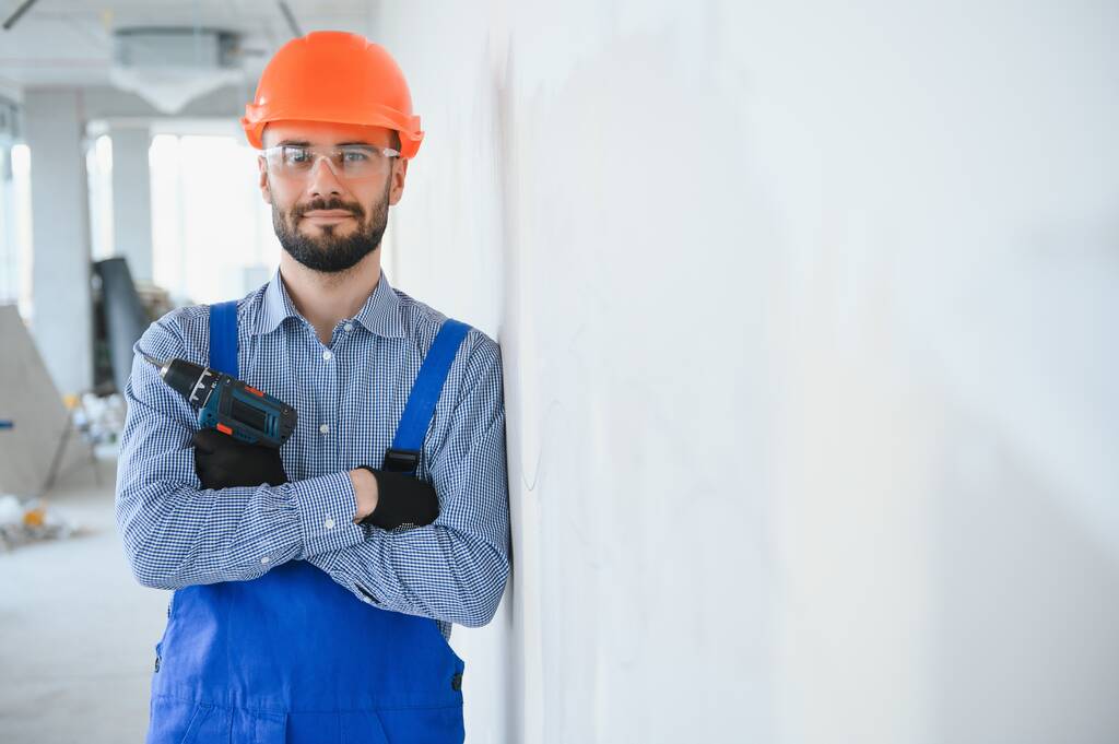 Portret van een jonge en hardwerkende constructeur die poseert in een grote onvoltooide ruimte. Bouwconcept. - Foto, afbeelding