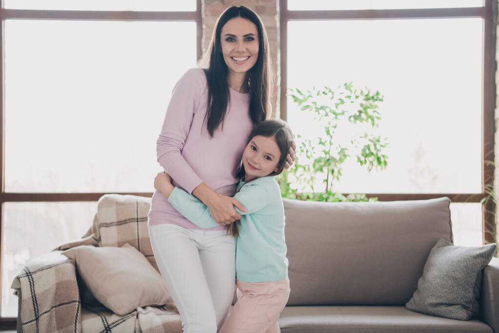 Фотопортрет очаровательной мамы обнимает маленькую дочь провести выходные свободные каникулы вместе возле диван квартиры. - Фото, изображение
