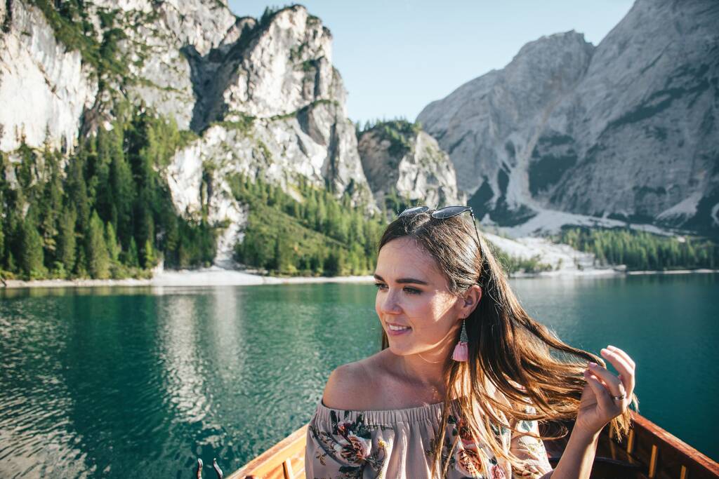 Een vrouwelijke toerist die met haar haar speelt en geniet van het prachtige uitzicht op een houten boot op Lake Braies, Italië - Foto, afbeelding