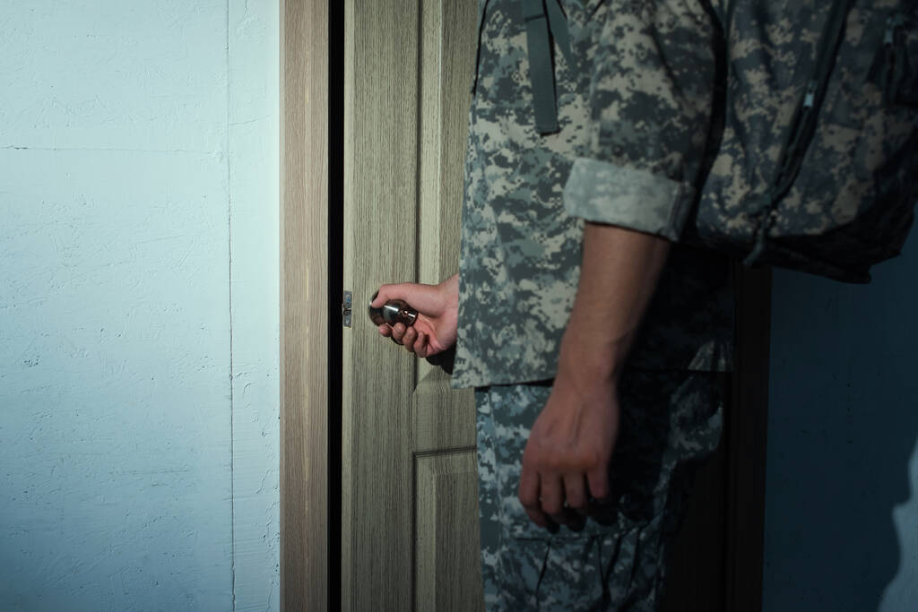 vue recadrée du militaire en camouflage ouvrant la porte de la maison - Photo, image