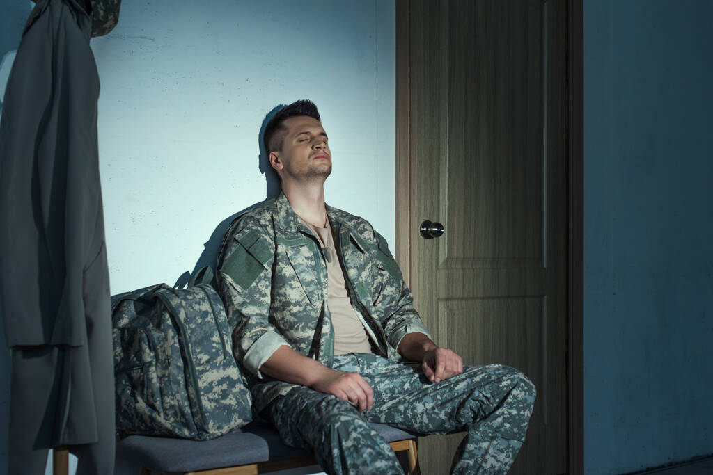 Wojskowy żołnierz z niepokój siedzi w korytarzu na ławce w nocy  - Zdjęcie, obraz
