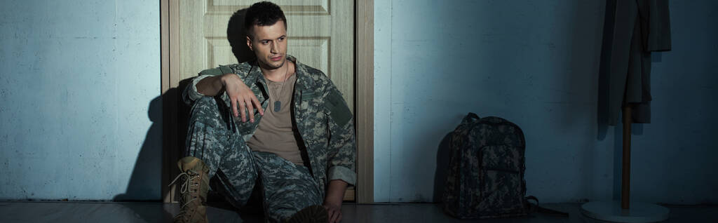Soldat avec trouble de stress post-traumatique assis près de la porte dans le couloir à la maison, bannière  - Photo, image