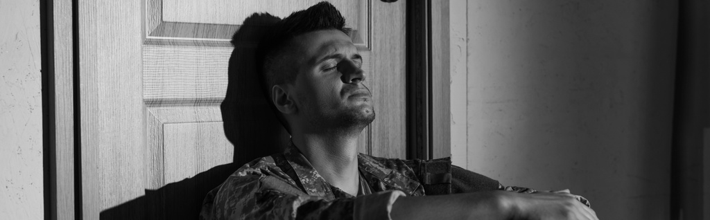 Photo en noir et blanc d'un vétéran militaire avec traumatisme psychologique assis près de la porte à la maison, bannière  - Photo, image